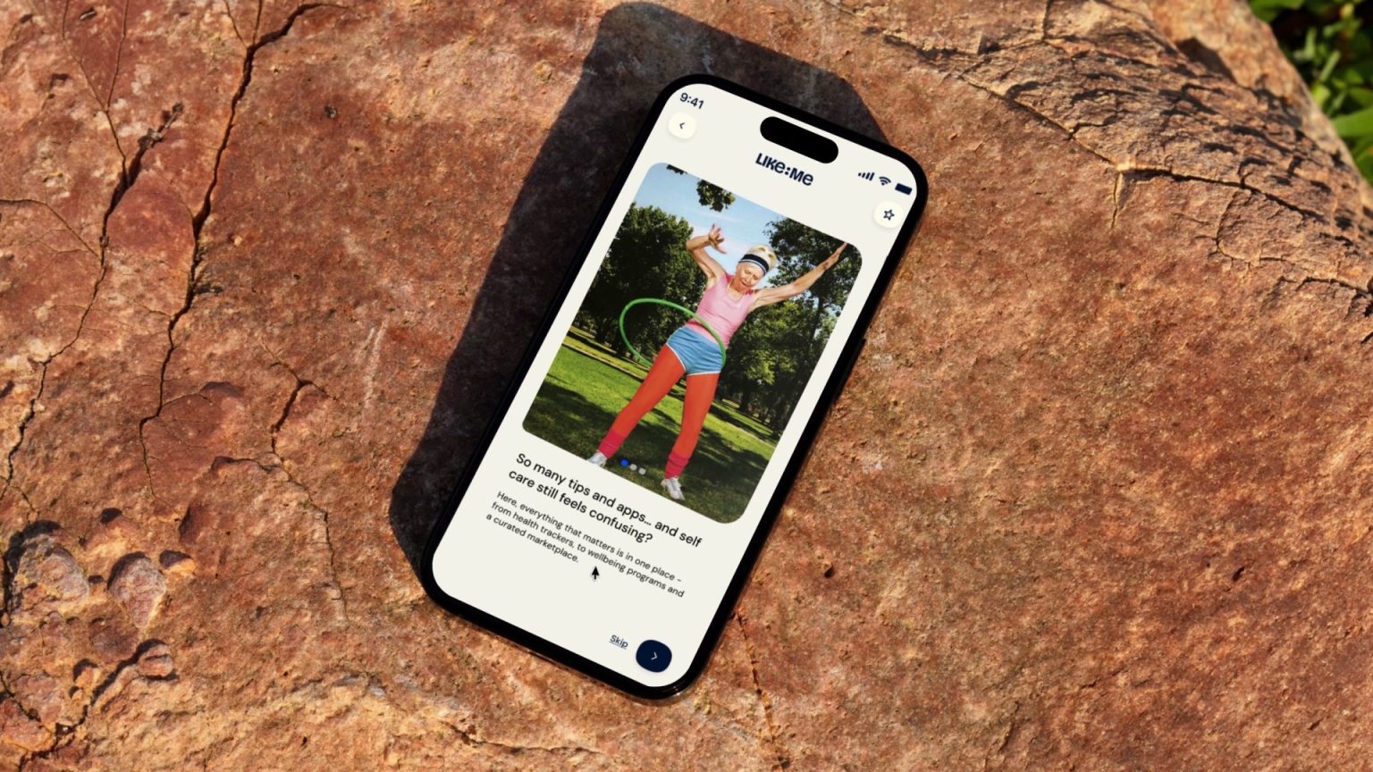 Celular sobre uma pedra com um slide de boas-vindas do Like:Me que reúne, num só lugar, acompanhamento de saúde, programas de bem-estar e um marketplace com curadoria